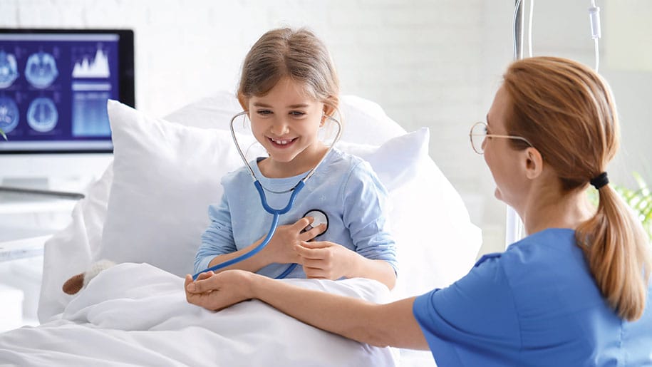 smiling young girl in hospital bed with nurse and stethoscope